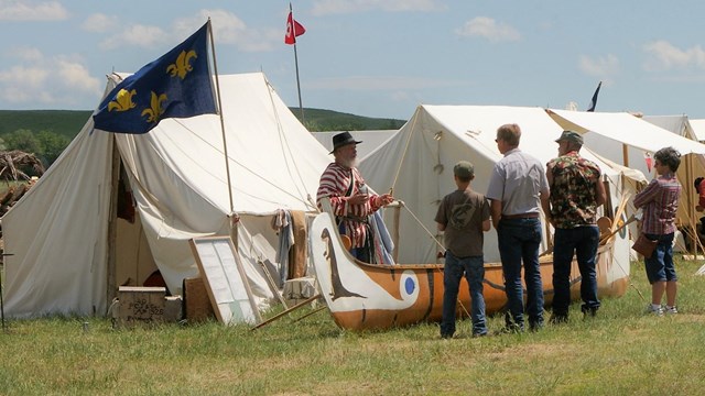 Man stands behind birchbark canoe talks to visitors